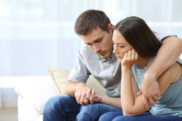 Pregnancy loss - Sad couple comforting each other sitting on a couch